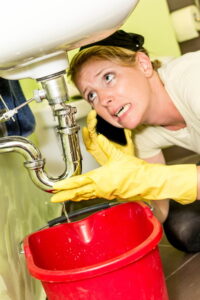 woman-looking-under-sink-with-bucket-to-catch-leak