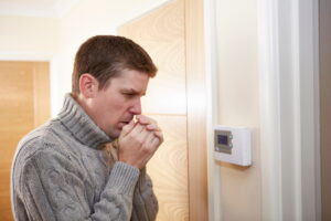 man-standing-in-front-of-thermostat-blowing-into-hands
